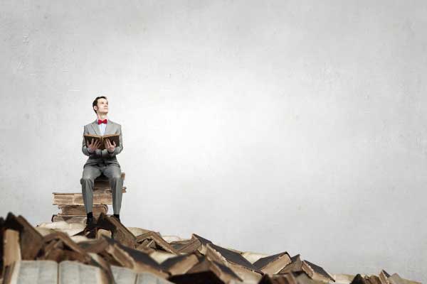 Man sitting on top of books reading a book